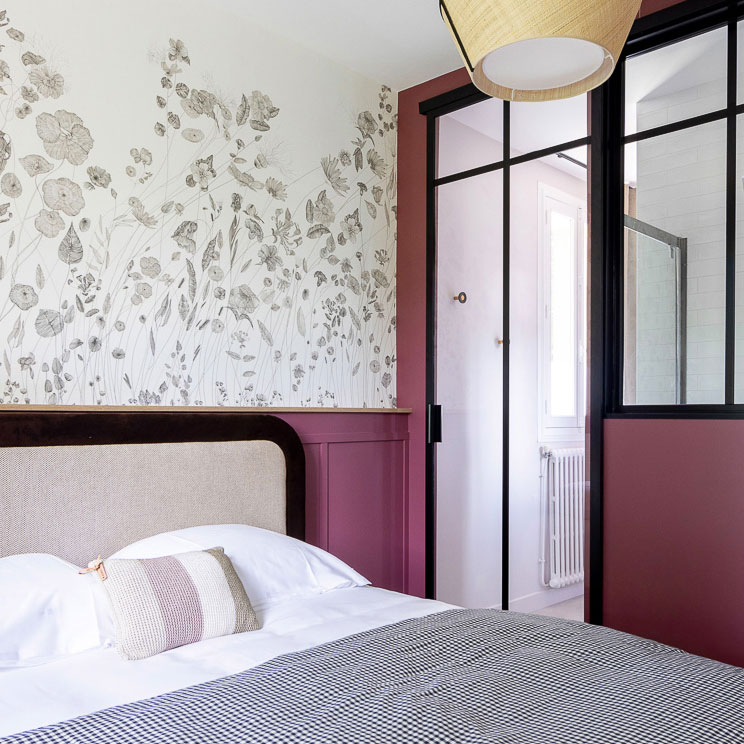 Chambre avec salle de bain séparées par une verrière qui laisse passer la lumière et ouvre l'espace.